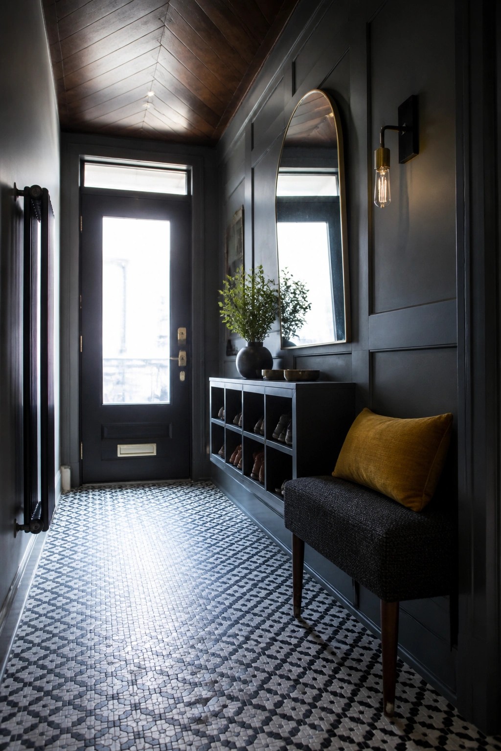 A narrow interior entryway with a dark wood chevron ceiling, dark paneled walls, a black front door, mosaic tile floor, and a bench with a yellow pillow.