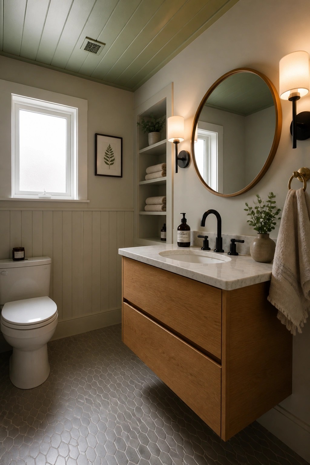 A bathroom interior with a painted tongue and groove ceiling, white wainscoting, a floating wood vanity, round mirror, and hexagon tile floor.