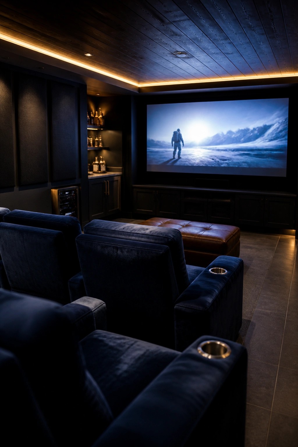 Navy velvet recliners face large screen showing snowy landscape in dark theater room