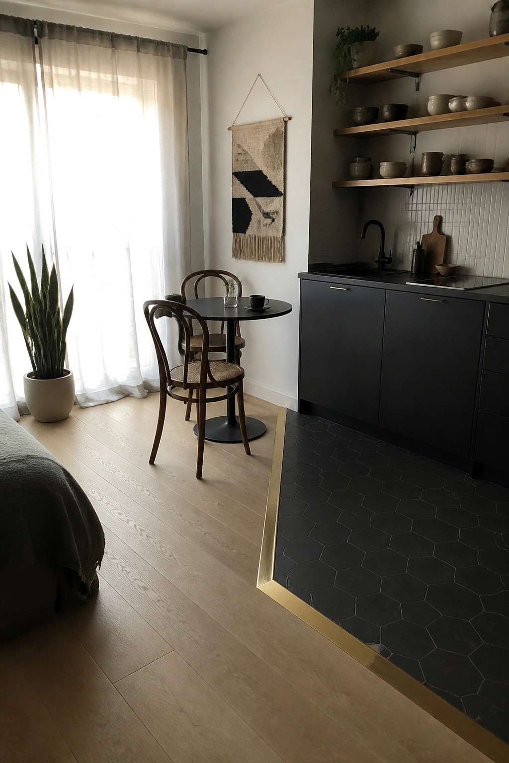 Light wood flooring transitions to dark hexagonal tile via a brass strip, with a round table and chairs on the wood side and dark cabinets on the tile side.