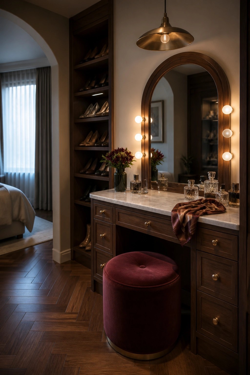 Elegant dark wood vanity with marble top, arched lit mirror, red velvet stool, and perfumes.