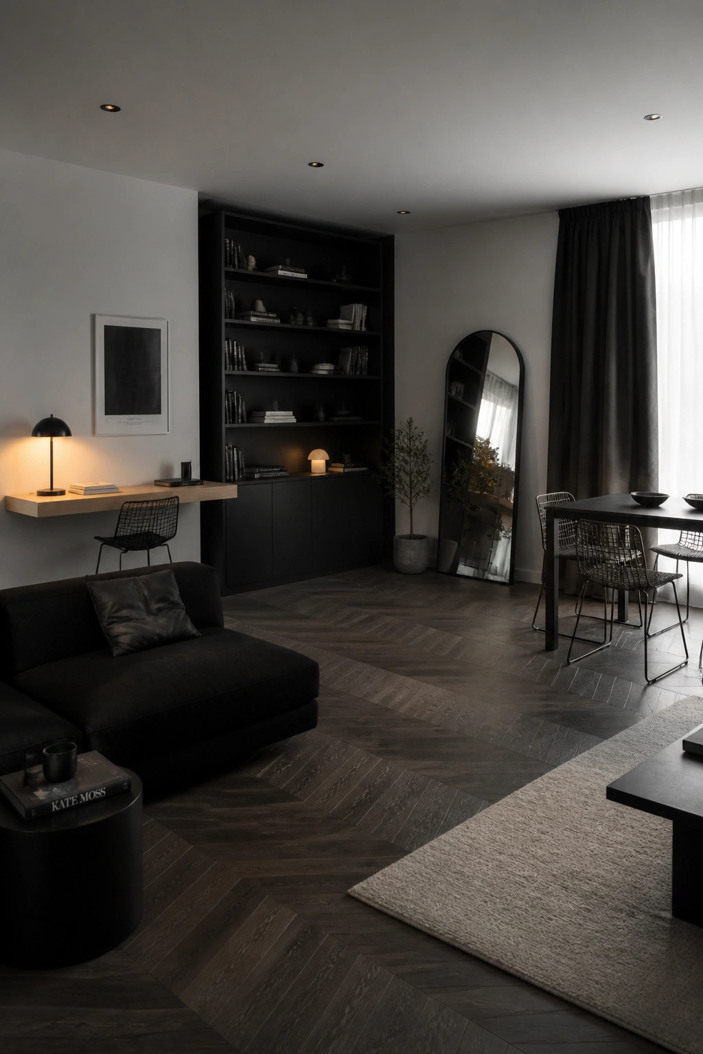 A modern open concept living and dining space featuring dark herringbone wood flooring, black built-in shelving, a dark sectional sofa, and a dining table with wireframe chairs.