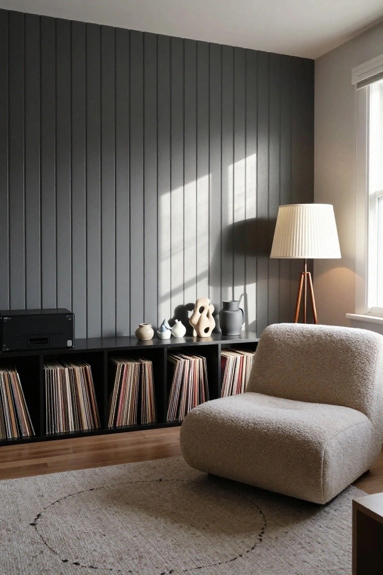 A room with a dark vertical wood slat accent wall above a low black record cabinet, a beige armchair, and a floor lamp.