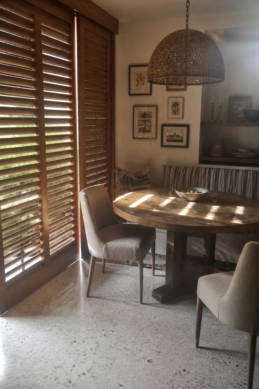 Round wooden table with beige chairs under woven pendant light by shutters