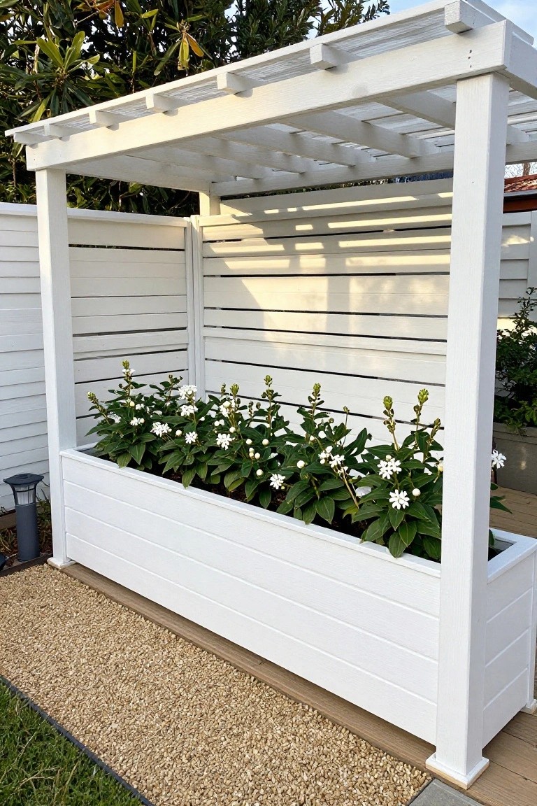 White wooden planter box with white flowers under slatted pergola on gravel patio