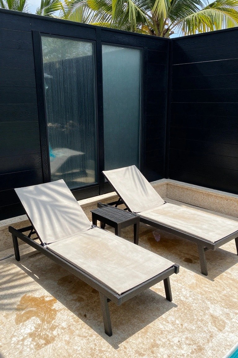 Two lounge chairs on a tiled patio beside a black wood fence with glass inserts.