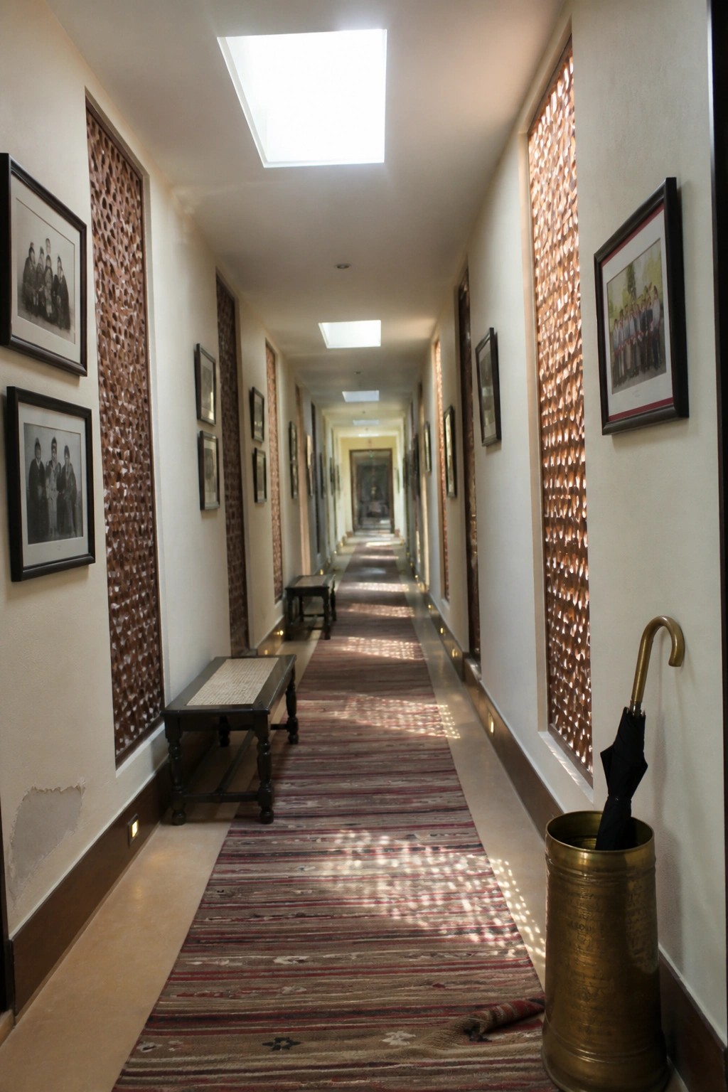 Long hallway with striped rug, wooden benches, framed photos, and umbrella stand